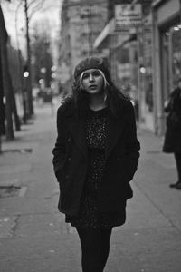 Portrait of young woman walking on sidewalk in city