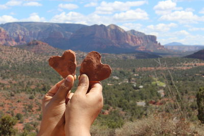 Cropped hand of person holding heart shape food against cloudy sky