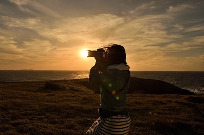 Man photographing on sea against sky during sunset