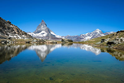 Scenic view of lake and mountains against clear blue sky