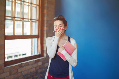 Woman yawning while standing against wall