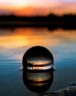 Close-up of crystal ball against lake during sunset