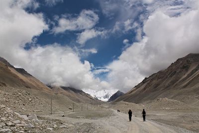 People walking on dirt road against sky