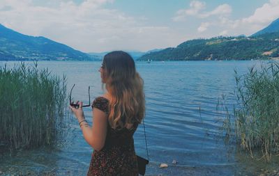 Rear view of woman standing by lake against sky