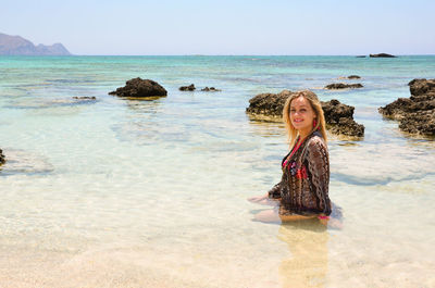 Young beautiful woman in shallow water by rocks.