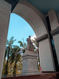 Low angle view of statue by palm trees against sky