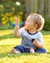 Cute baby boy sitting on grassy field at park