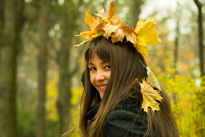 Portrait of smiling mid adult woman with autumn leaves on head at park