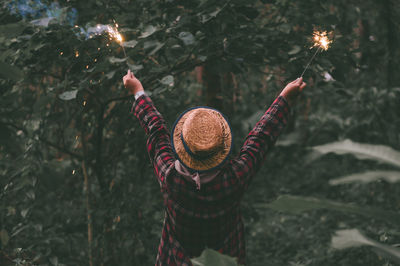 Rear view of woman holding illuminated sparklers while standing in park