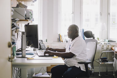 Mature male doctor working on computer while sitting at desk in clinic