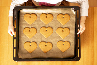 Many homemade fresh baked heart cookies on a baking sheet in the hands of a girl. concept.