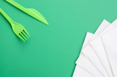 High angle view of plastic cutleries with tissue papers on green background