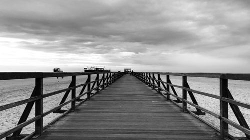 Wooden pier at beach against cloudy sky