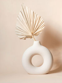 Round stylish ceramic vase with dried palm leaf casting shadows on the wall. beige background. 