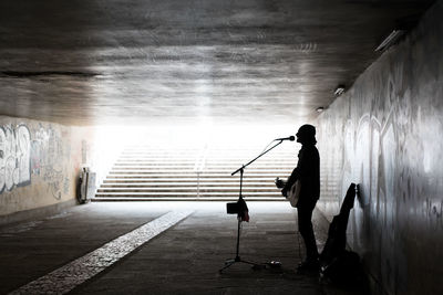 Silhouette of street musician playing guitar while singing at underground walkway