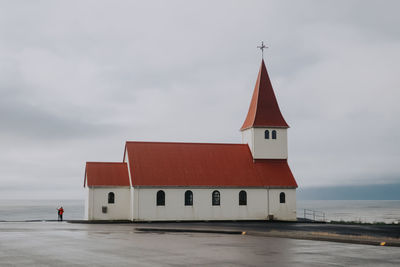Church by sea against cloudy sky