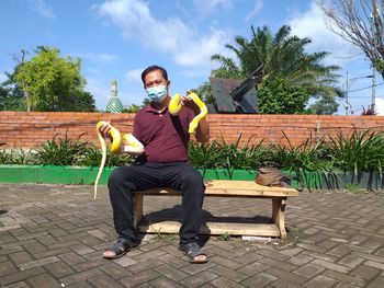 Full length of man with python sitting on bench