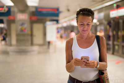 Smiling woman using mobile phone while standing at shopping mall