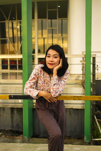 Portrait of smiling young woman standing against built structure