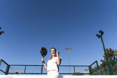 Excited young woman cheering at sports court on sunny day