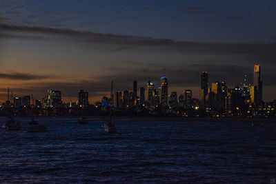 Illuminated city by sea against sky