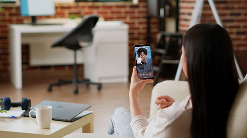 Rear view of woman using mobile phone at table