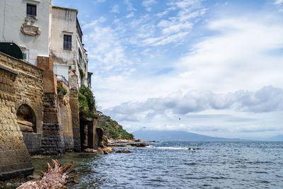 Buildings at sea against cloudy sky