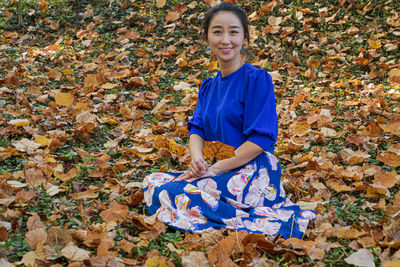 Portrait of smiling young woman sitting on autumn leaf