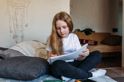 The girl after school plays at home, draws with pencils and felt-tip pens