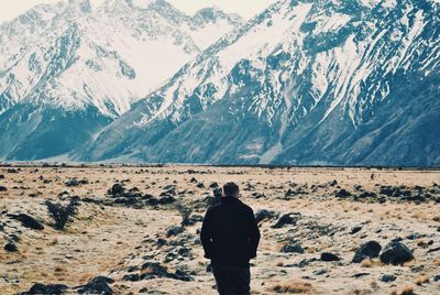 Rear view of man standing on cliff against mountains