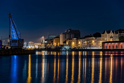 Illuminated buildings by river against sky in city at night