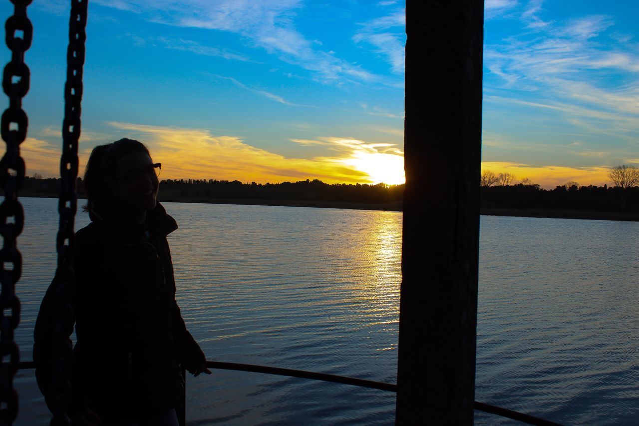 SILHOUETTE WOMAN STANDING BY LAKE AGAINST SKY