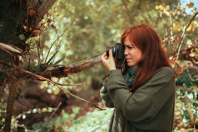 Young woman taking photos in the forest with an old analog camera