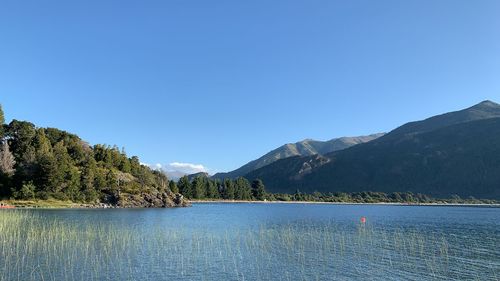 Scenic view of lake and mountains against clear blue sky