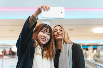 Multi-ethnic beautiful couple of girlfriends in a department store on the escalators take a selfie