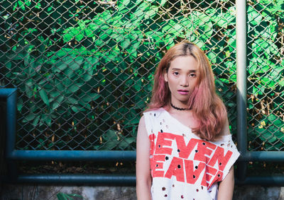 Portrait of young woman with long hair standing against fence