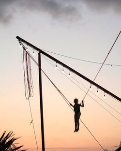 Low angle view of silhouette man walking on rope against sky