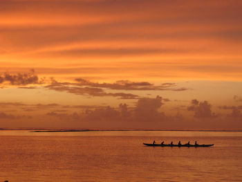 Six people paddling on canoe at sunset