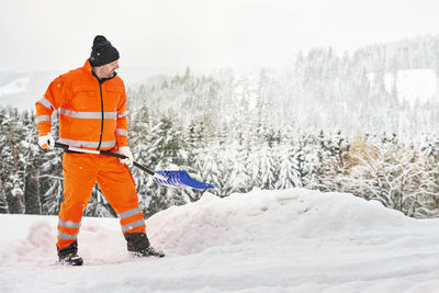 Communal service worker in uniform with a shovel clears snow in winter