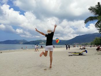 Rear view of cheerful woman dancing at beach against cloudy sky