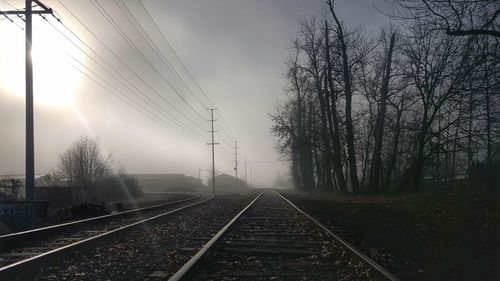 Railroad tracks by bare trees against sky