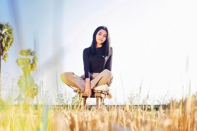 Portrait of smiling young woman sitting on field against sky