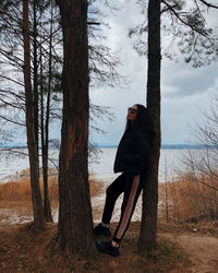 Portrait of young woman standing on tree trunk against sky