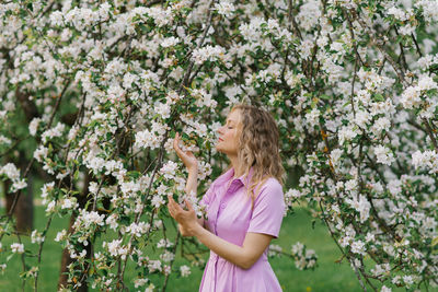Thirty year old woman sniffs a branch of a flowering tree in the park in spring