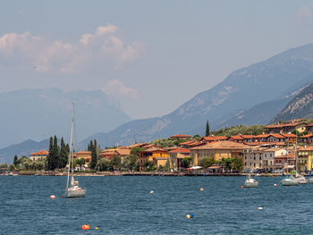 View of boats on the water and houses on the riva di guarda coastline, during summer, italy.