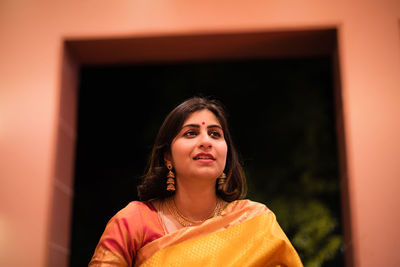 Smiling mid adult woman wearing sari and jewelries while looking away at home during night