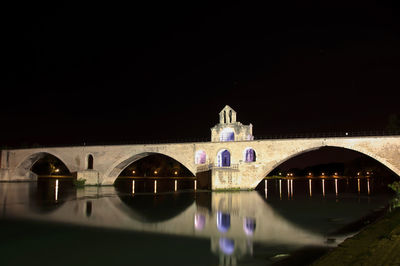 Arch bridge over river by building against sky at night