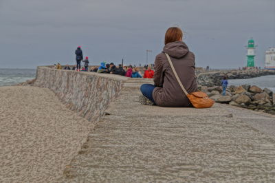 Rear view of woman sitting on retaining wall at shore