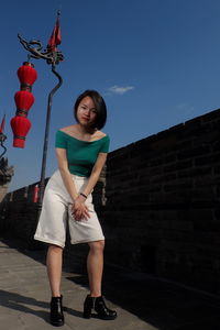 Portrait of young woman standing against blue sky