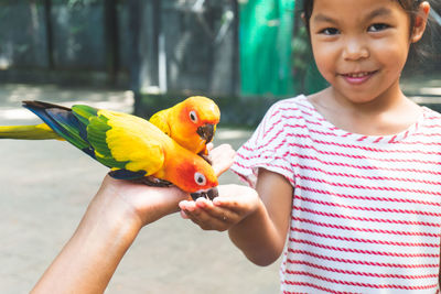 Portrait of girl feeding birds perching on hand